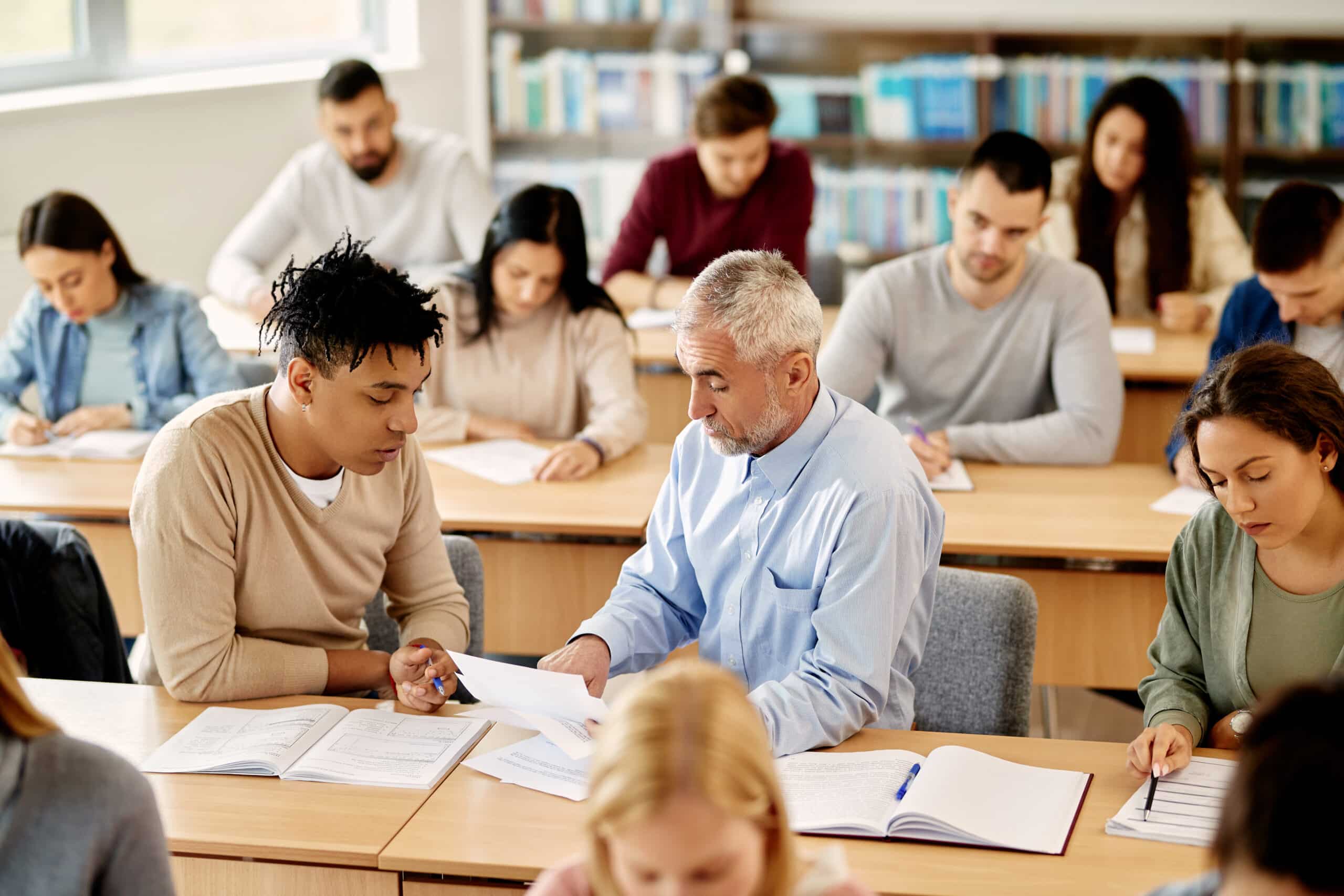 TAE40122 - Mature teacher talking to his student while assisting him with the lecture in the classroom.