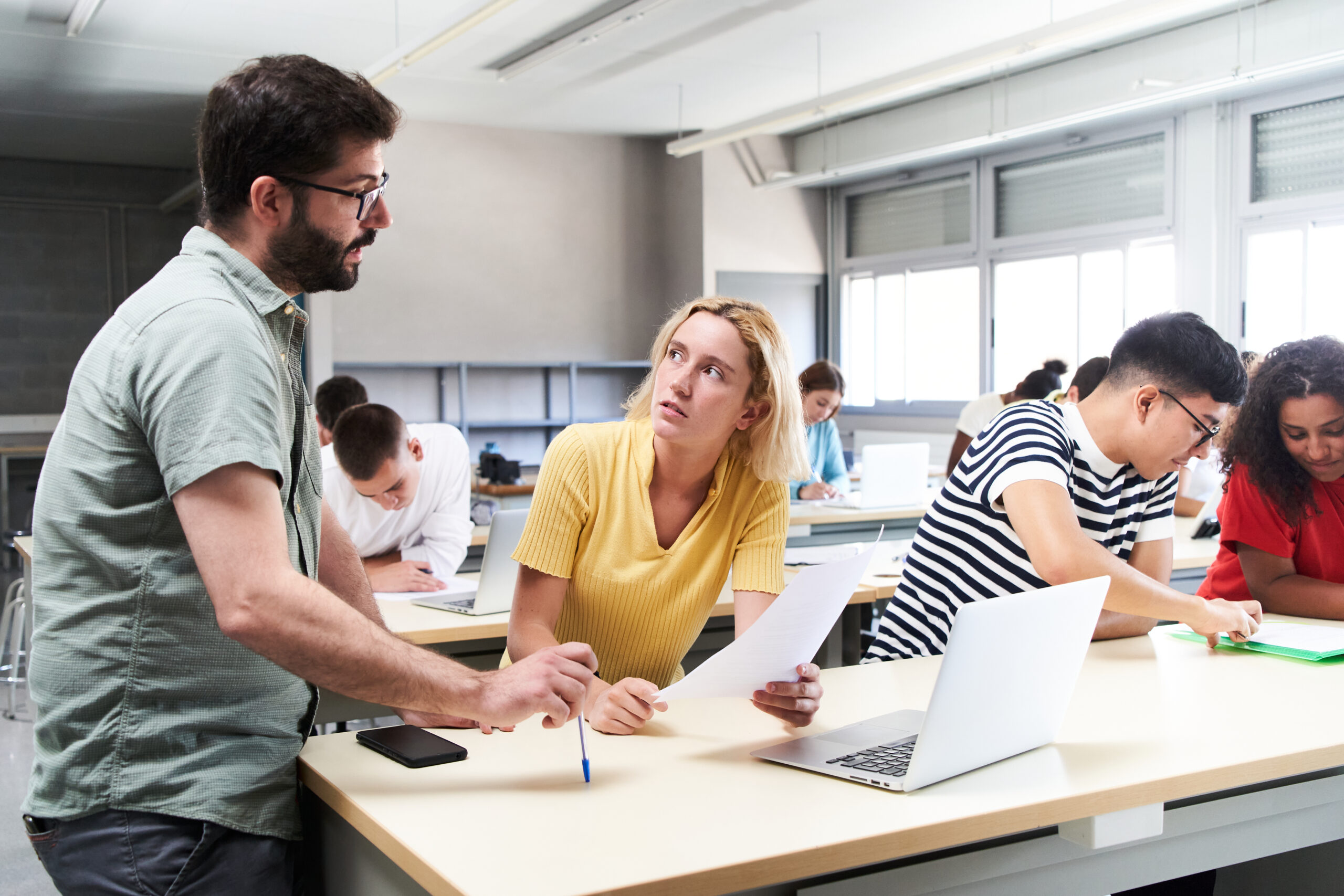 Adult learners - Young male teacher helping female student in class. The tutor helping his students by explaining the lesson and solving doubts. High quality photo