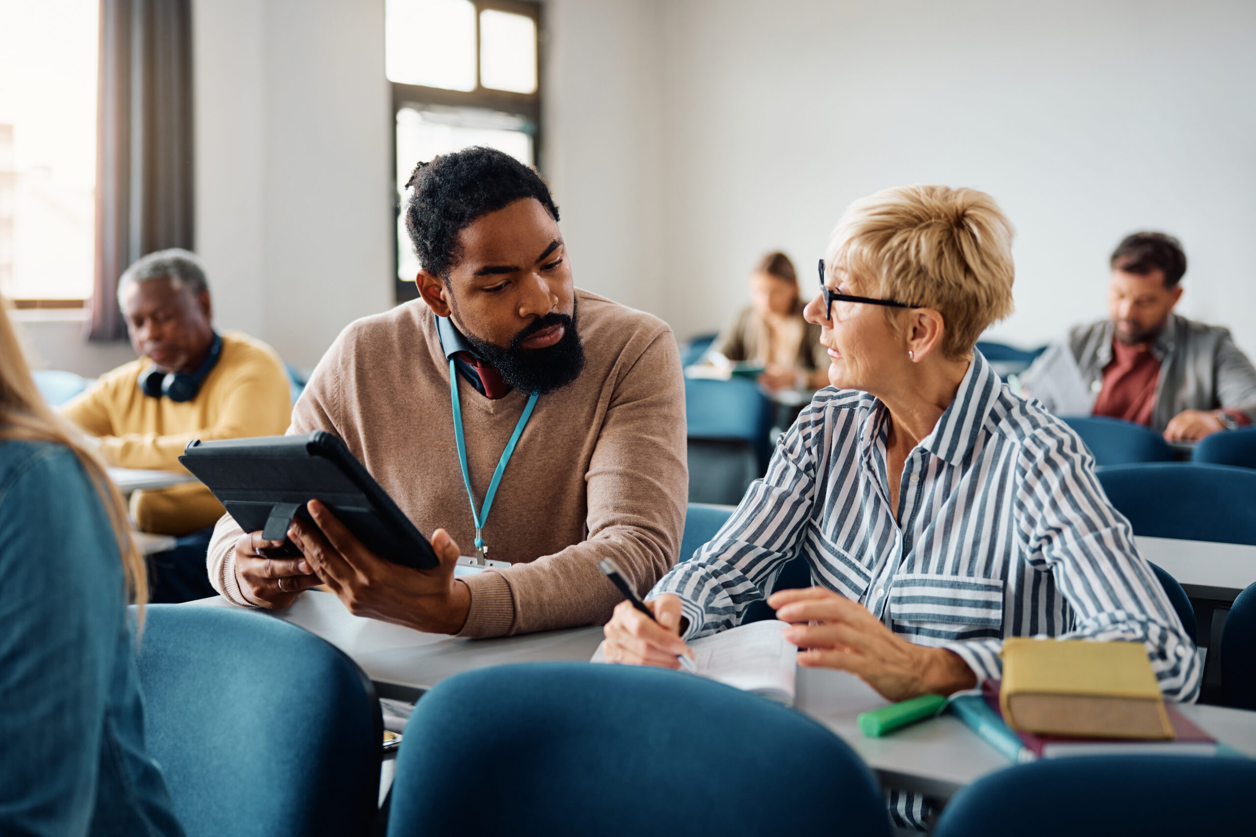 TAE - Mature woman talking to African American teacher while studying during adult educational training class in the classroom.